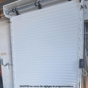 Porte de garage en aluminium enroulable sur mesure en cours de réglages et programmation sur banc de test